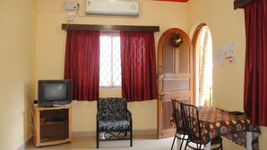 Una habitación con un televisor sobre un soporte de madera, una silla estampada, una mesa con mantel floral y una puerta decorada con un adorno.