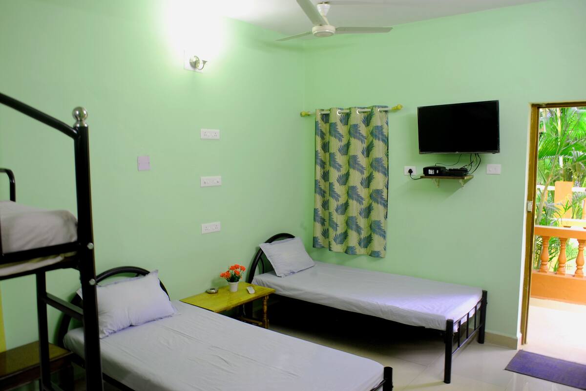 A room with bunk beds, a single bed, a TV mounted on the wall, and a curtain with a leaf pattern.