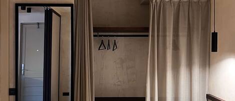 A hotel room with a bed, a bench, a mirror, and curtains.