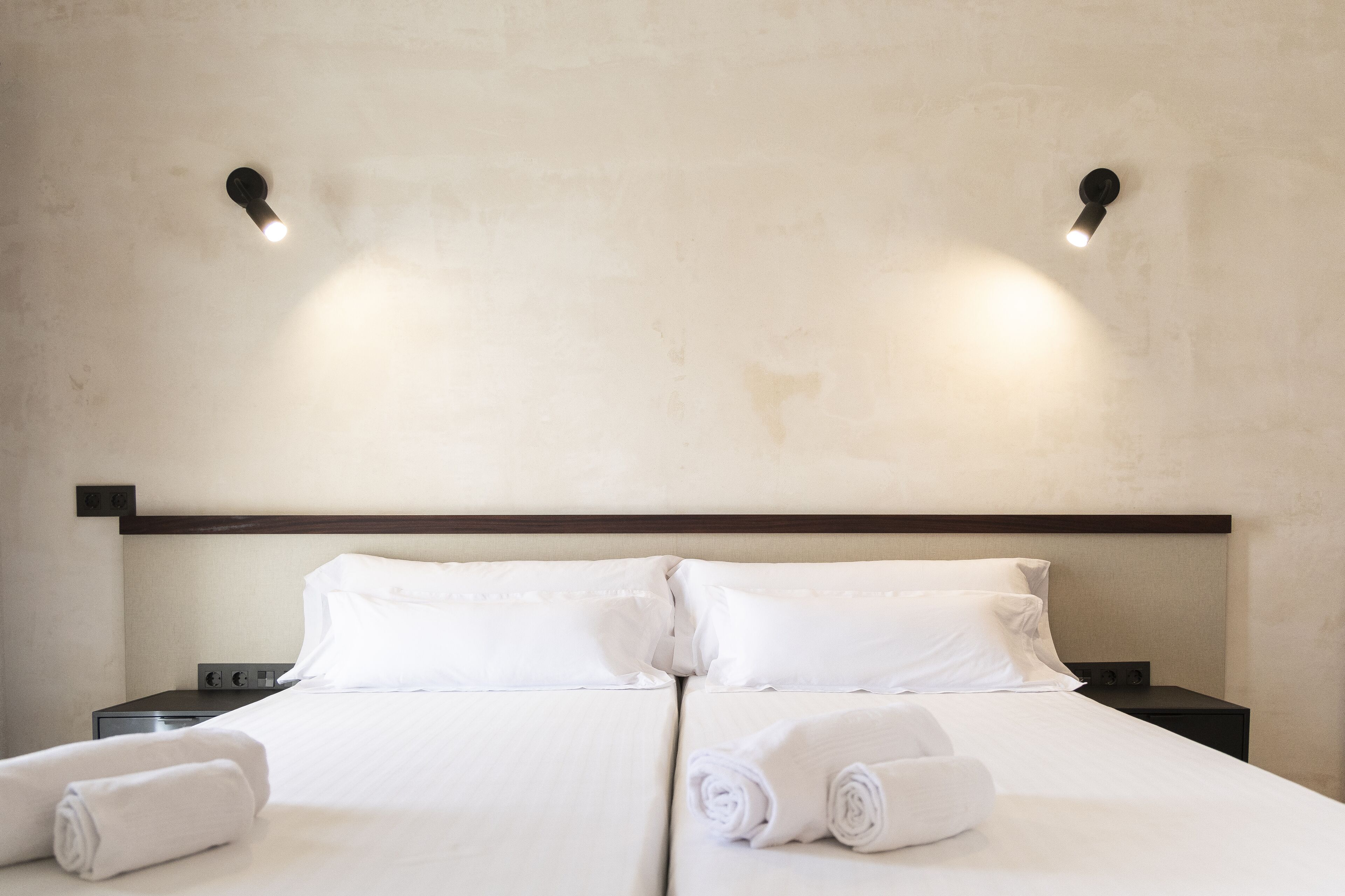 Habitación de hotel con cama doble, dos mesitas de noche y dos luces fijadas a la pared.