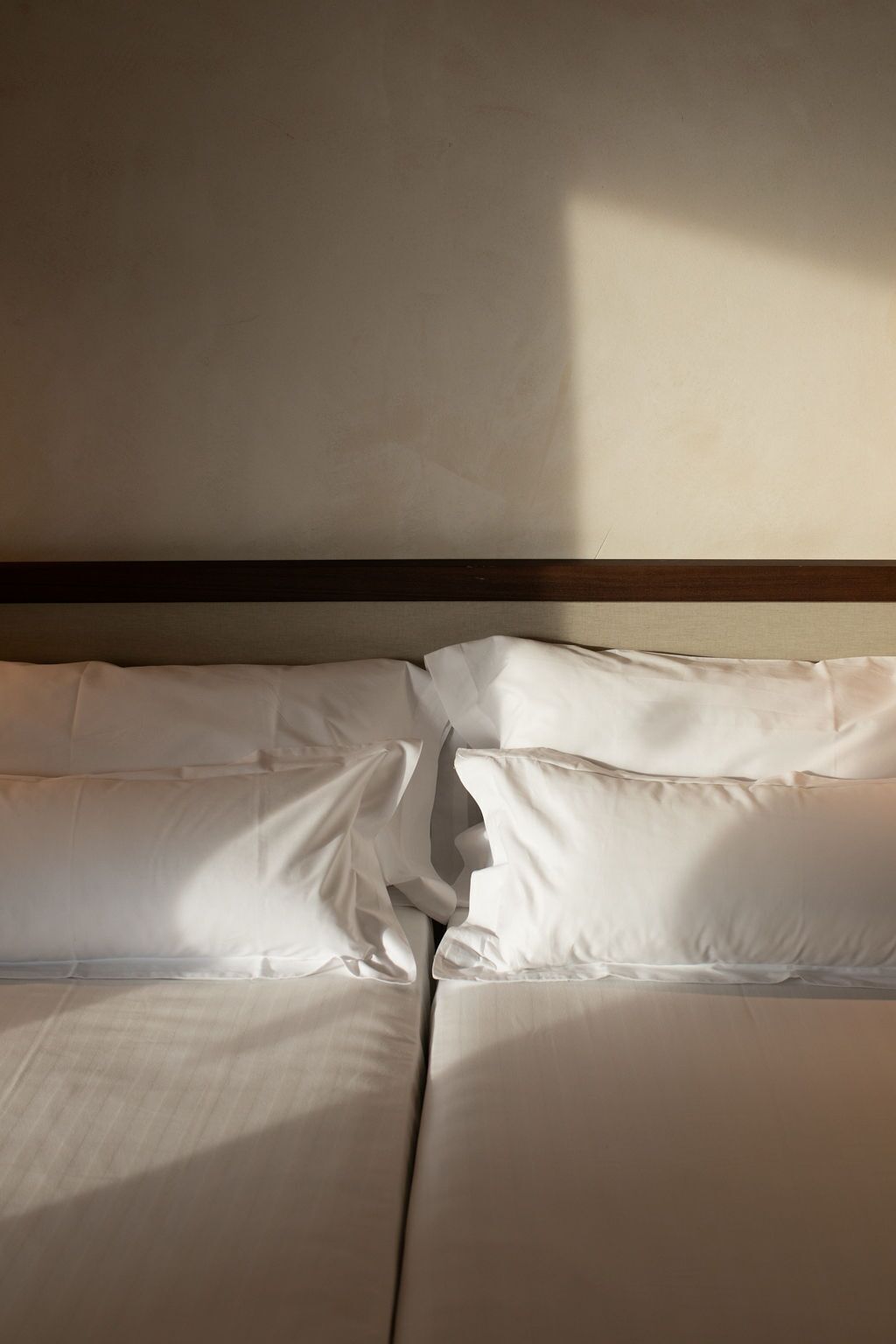A neatly made bed with white linens and a wooden headboard.