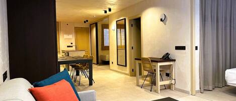 A modern hotel room with a sofa, a coffee table, a desk, and a dining area.