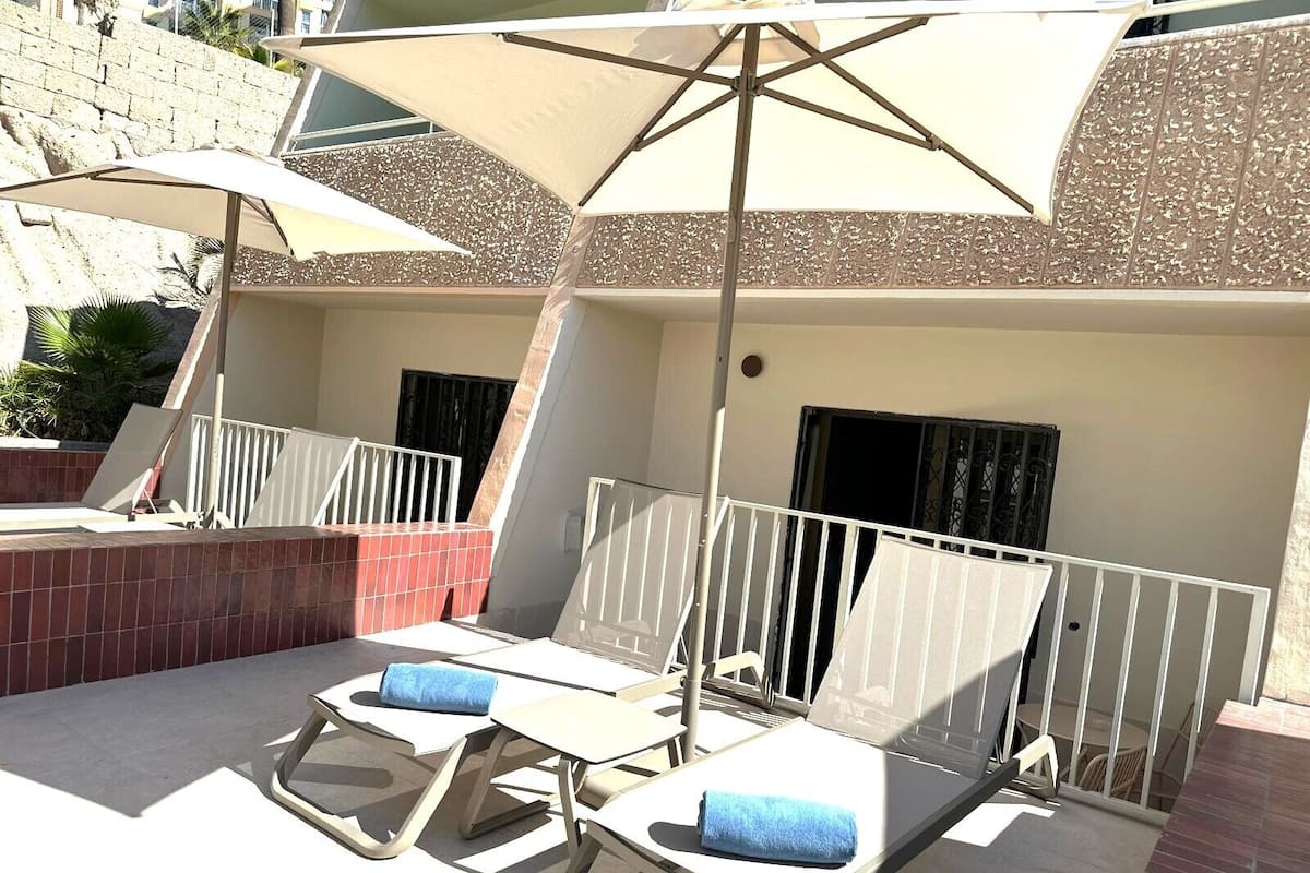 A rooftop terrace with two lounge chairs and a large umbrella.