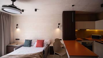 Una habitación de hotel moderna con una cama, mesitas de noche, un escritorio, una silla, una kitchenette y un ventilador de techo.