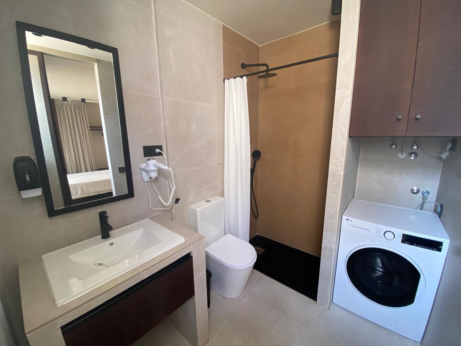 A compact bathroom with a sink, toilet, shower, and a built-in washing machine.