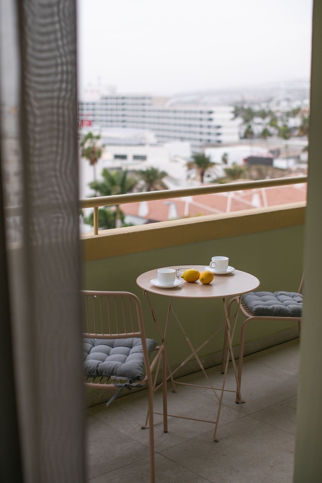 A balcony with a table set for two, two cups, and two lemons.
