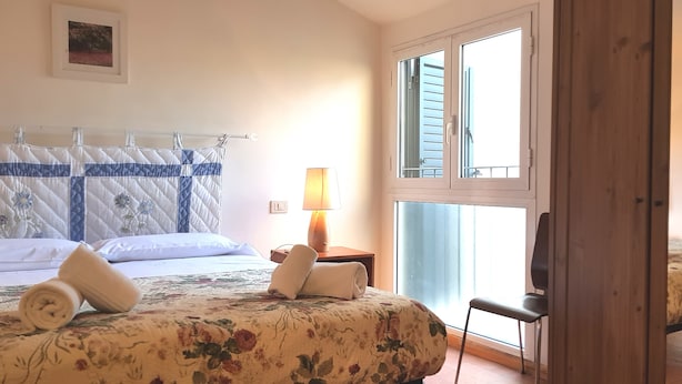 A hotel room with a bed, a chair, a lamp, and a window. - Appartamento Dante (Florence)