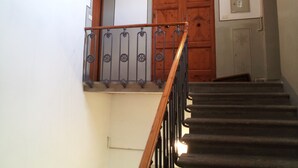 A staircase with a wooden handrail and metal balusters, leading to a wooden door with a decorative panel. - Appartamento Dante (Florence)