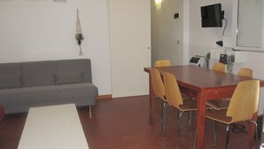 A room with a grey sofa, a wooden dining table with four chairs, a TV mounted on the wall, and a small plant on the wall. - Appartamento Dante (Florence)