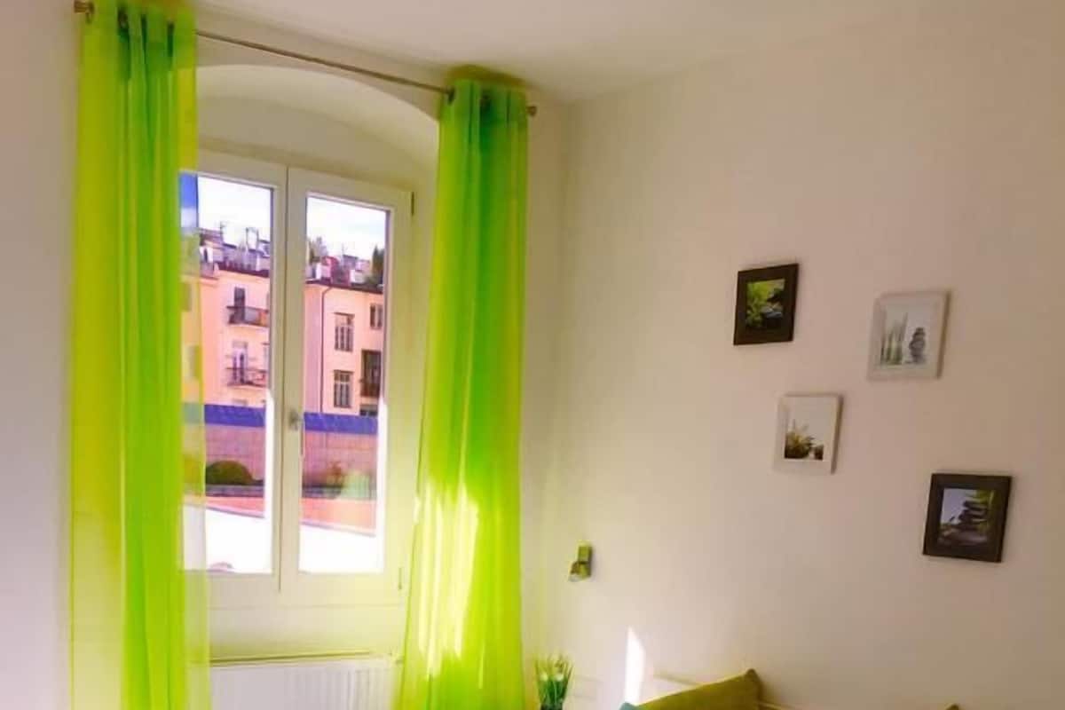 Una cama doble con dos almohadas, una mesita de noche y una ventana con cortinas.
