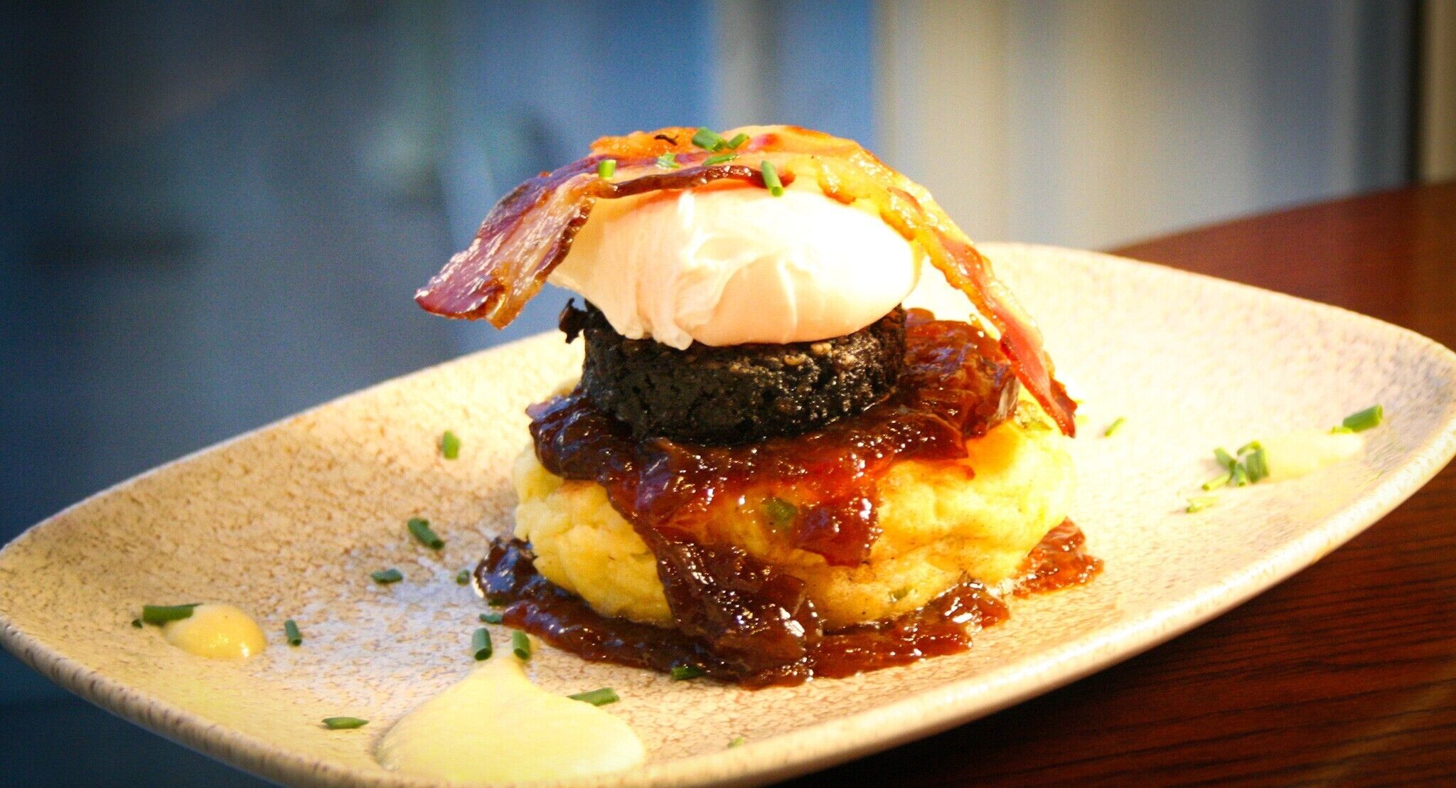 A dessert with a poached egg on top, served on a plate with a side of sauce and garnished with herbs.