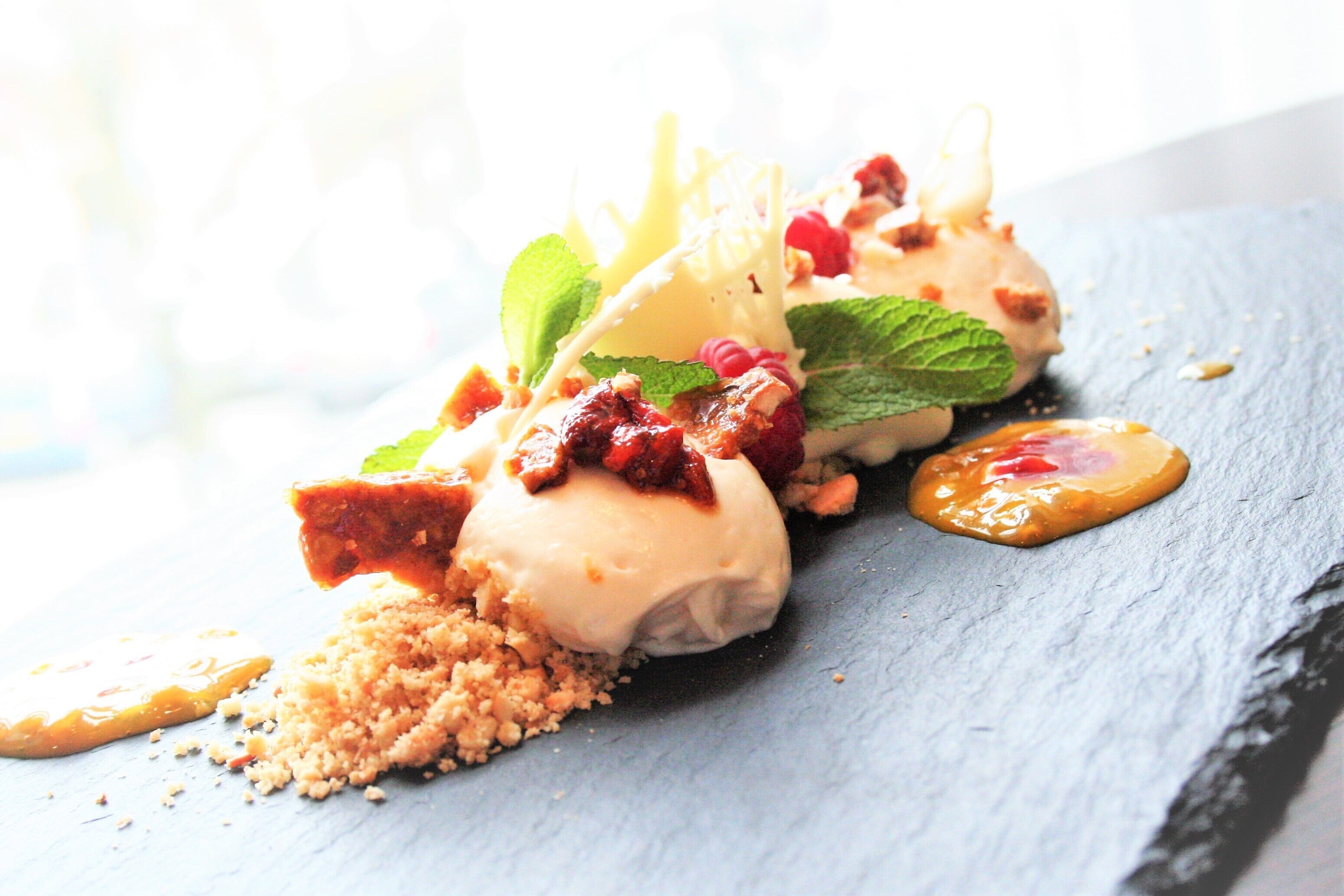 Un dessert servi sur une assiette en ardoise, avec une garniture croustillante et des feuilles de menthe.
