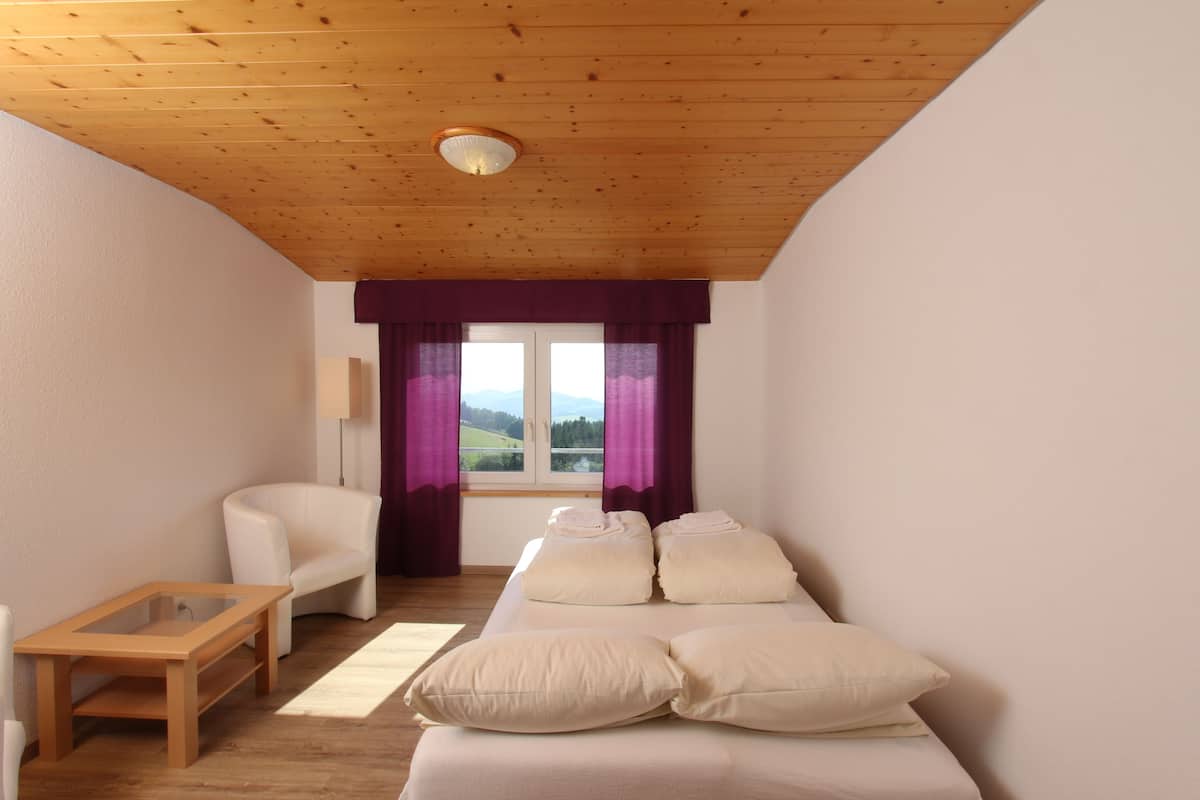 A room with a wooden ceiling, a white sofa with pillows, a small wooden table, and a window with purple curtains.