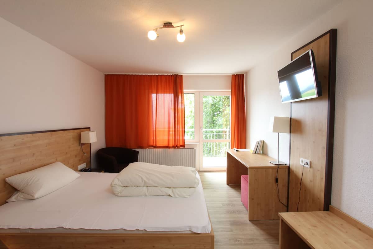 A hotel room with a bed, a desk, a chair, a TV, and a window with curtains.
