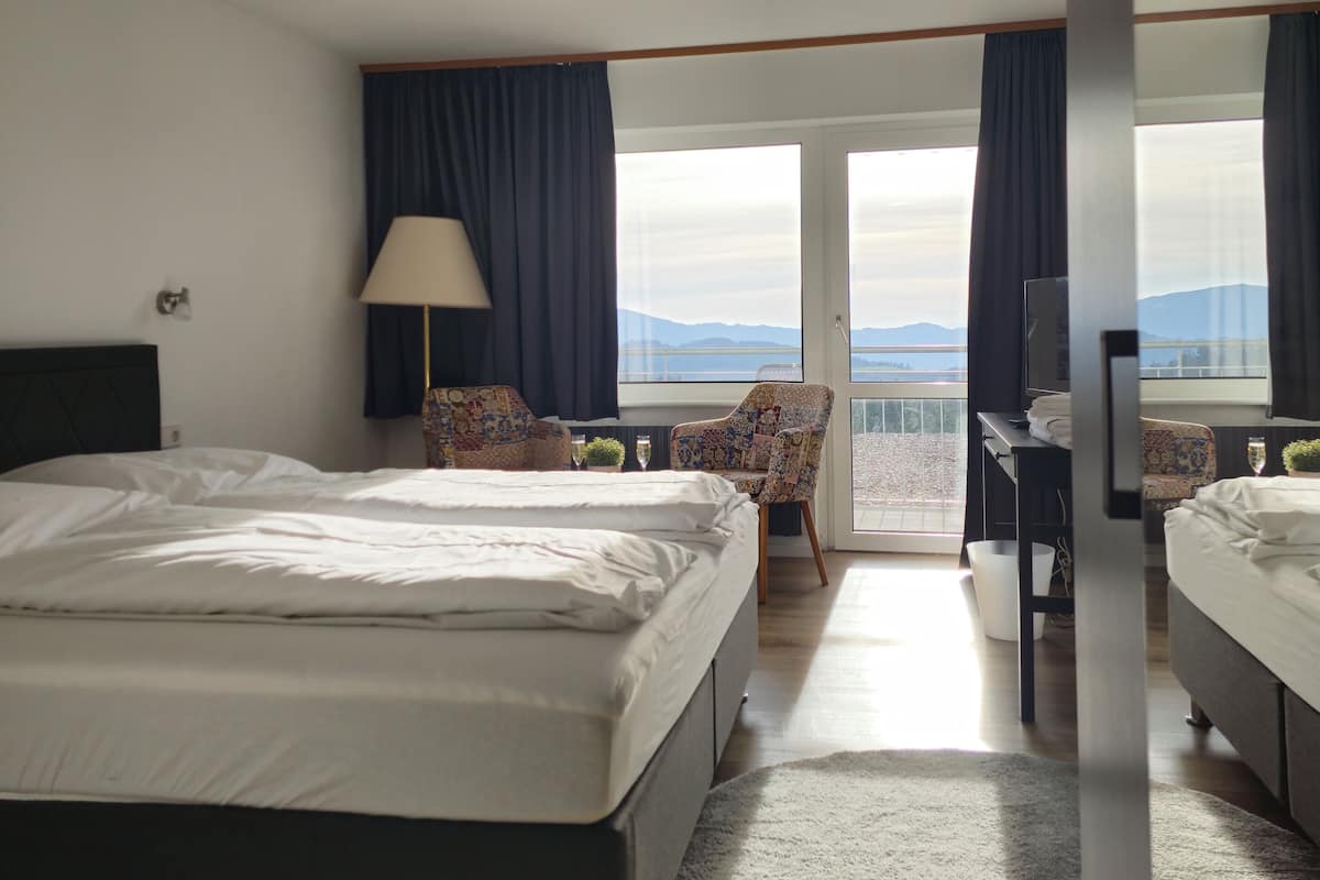 A hotel room with a bed, a chair, a desk, and a view of the mountains.