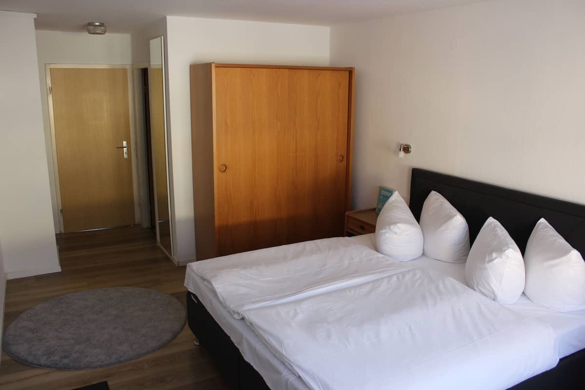 A bedroom with a bed, a wooden wardrobe, a bedside table, and a grey rug.