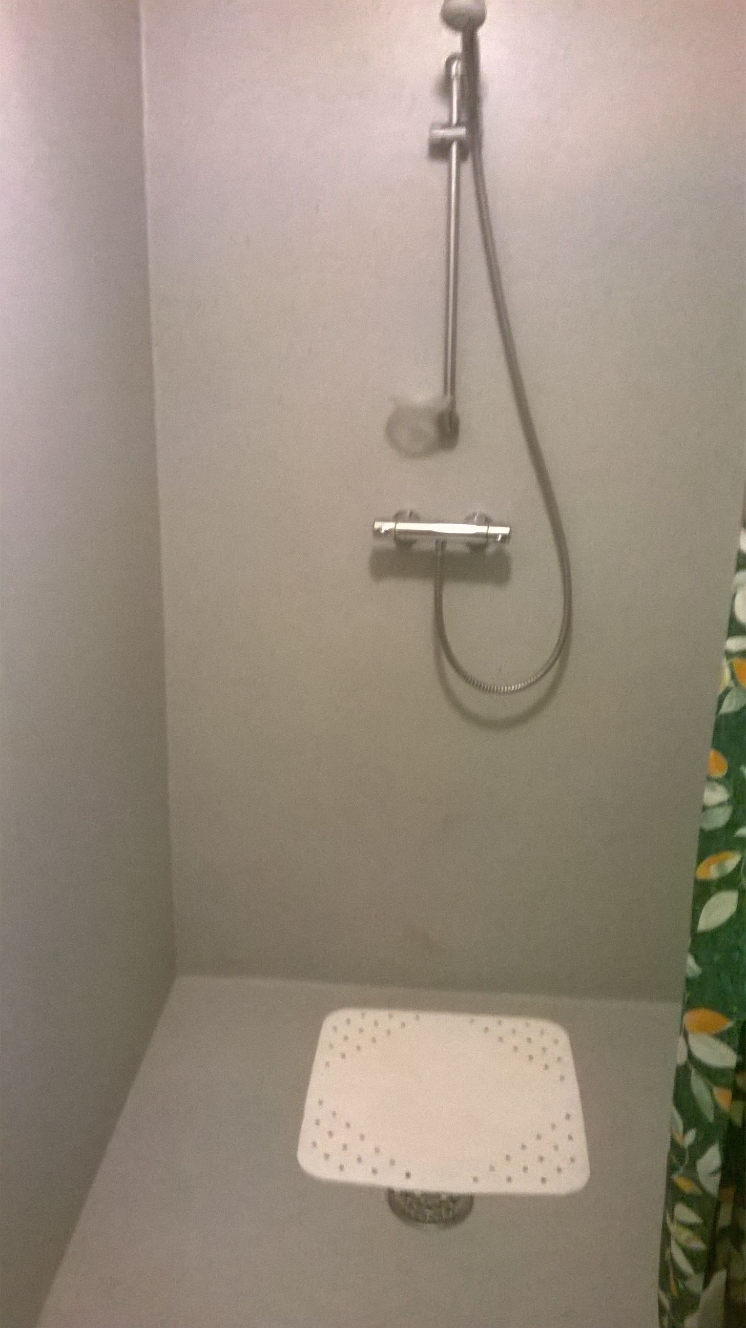 A small, enclosed shower area with a white shower seat and a handheld showerhead.