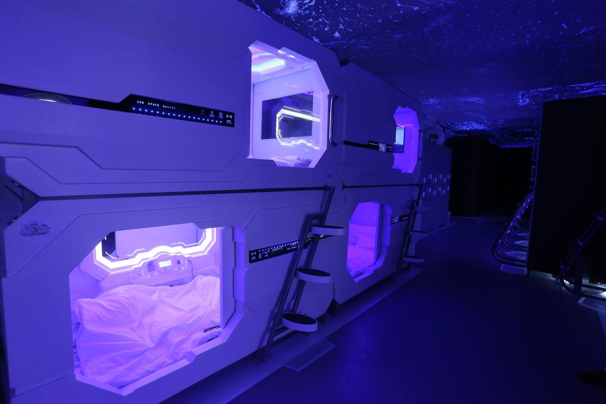 A futuristic room with multiple beds, each illuminated with blue lighting, and a control panel above one bed.