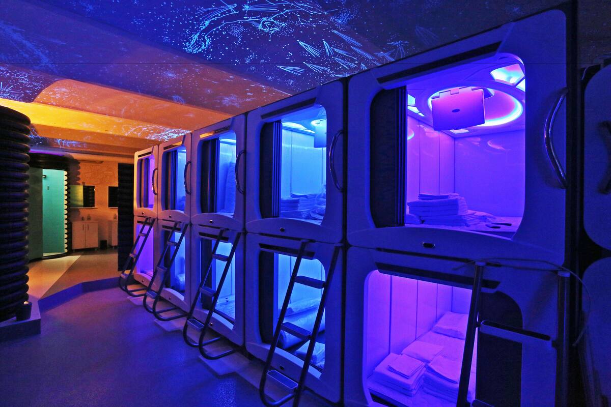 A row of capsule-style rooms with a starry ceiling projection, each with a ladder and a small table.