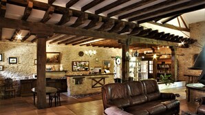 Een rustiek interieur met zichtbare houten balken, een stenen muur, een leren bank, een bar en een open haard.