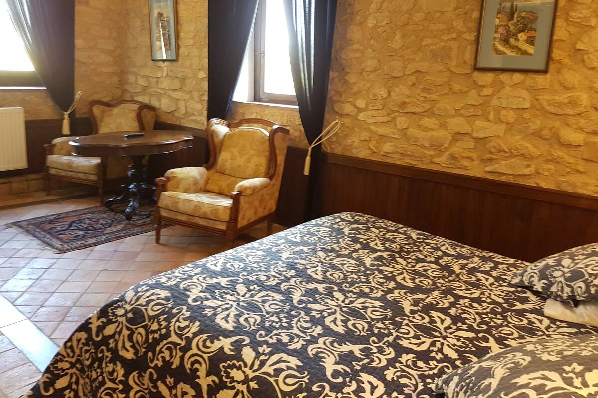 Une pièce comprenant un lit, une chaise, une table et une fenêtre avec des rideaux.