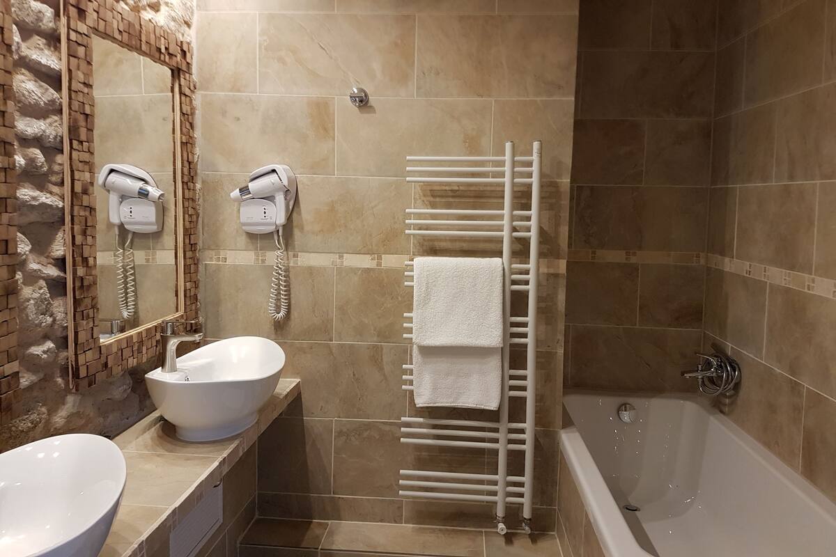 Une salle de bain avec un grand miroir, un lavabo, un porte-serviettes, un sèche-cheveux et une baignoire.