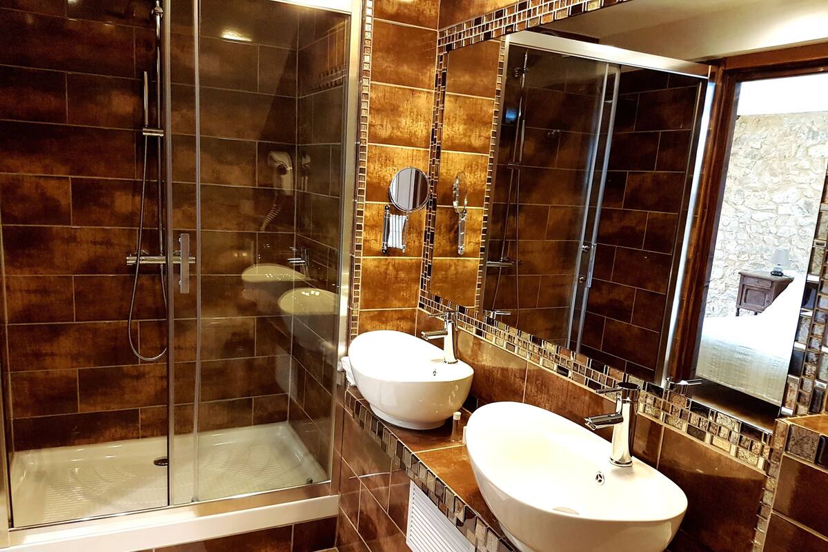 Une salle de bain moderne dotée d’une douche à parois de verre, de deux lavabos et d’un grand miroir.