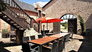 Een terras buiten met een houten tafel en stoelen, een rode parasol en een stenen muur.