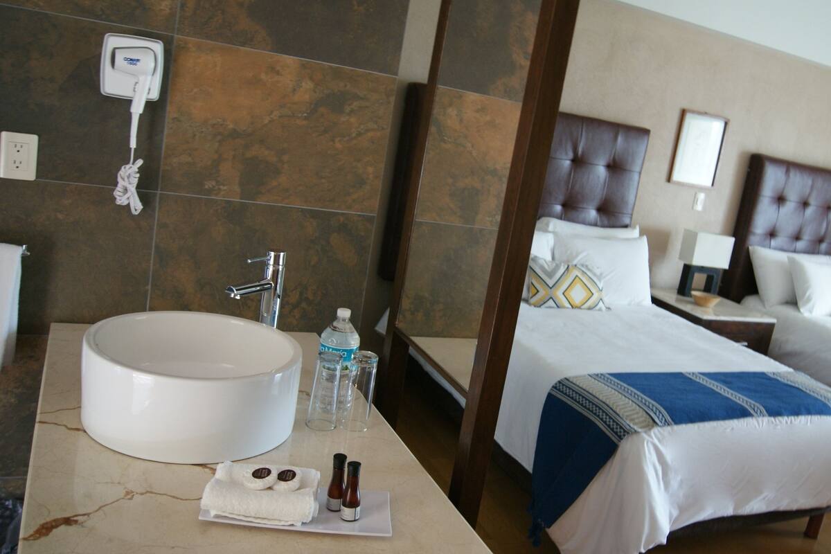 A hotel room with a large bathroom sink, a mirror, a towel, and toiletries. There are two beds with headboards and pillows.