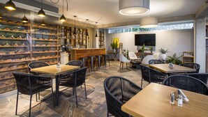 Un restaurante con una bodega de vinos, mesas de madera, sillas de mimbre negro y una zona de bar.