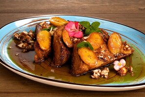 A plate of food with slices of meat and orange slices, garnished with herbs and flowers.