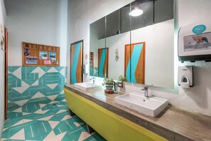A bathroom with two sinks, a mirror, a bulletin board, and a soap dispenser.