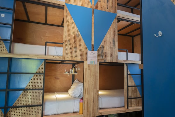 Habitación con literas de madera, pared azul y colchón blanco.
