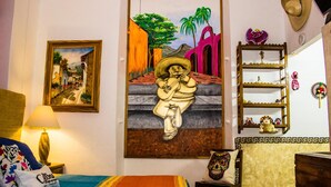 Una habitación con una cama, un cuadro de un hombre tocando guitarra, un estante con adornos y una pared con un cuadro enmarcado.