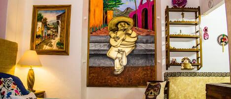 A room with a bed, a painting of a man playing guitar, a shelf with decorative items, and a wall with a framed picture.
