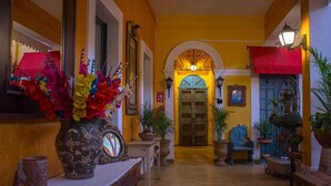 Un pasillo con pared amarilla, un banco de madera, una mesa con un jarrón de flores y una puerta con toldo rojo.
