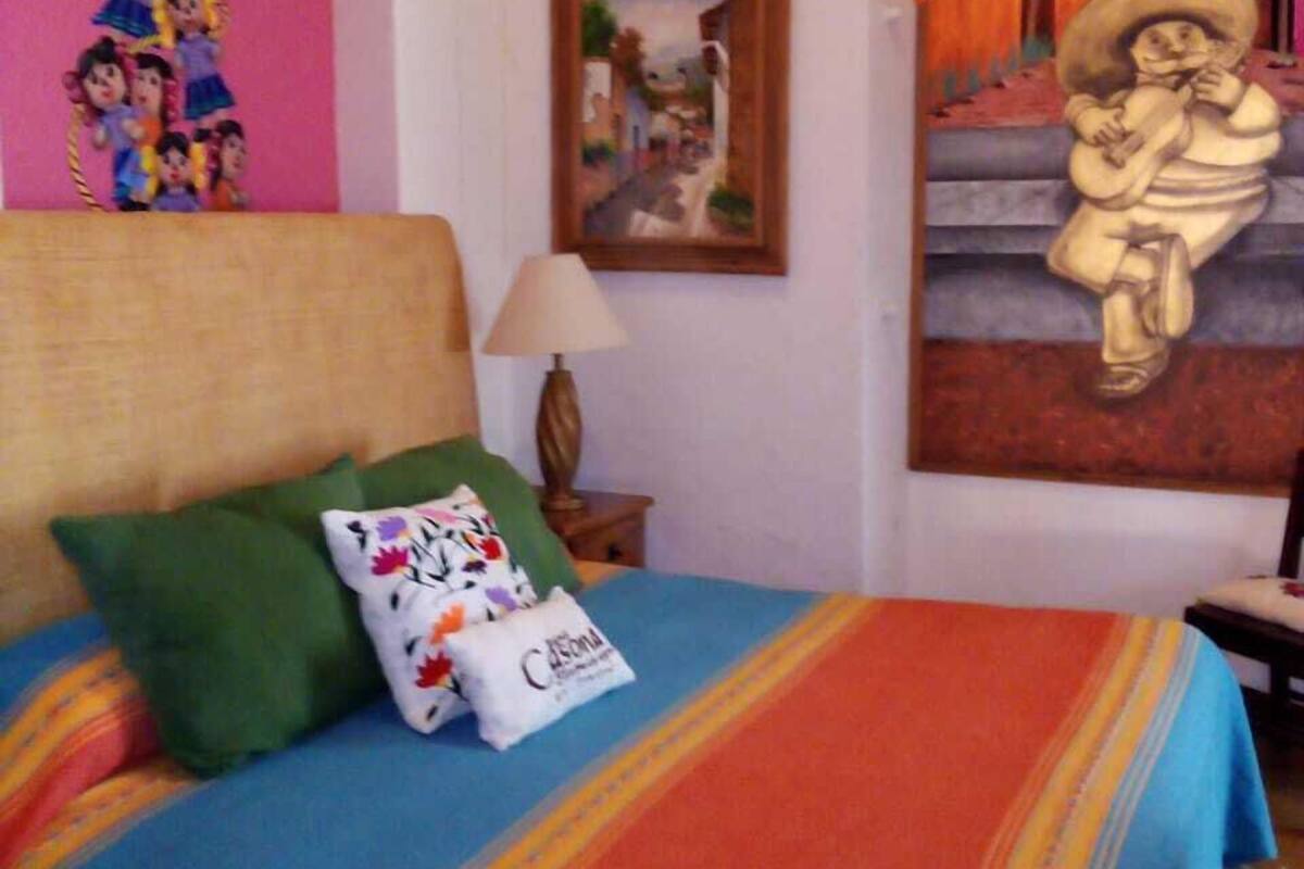 Un lit avec une literie aux couleurs vives, un oreiller orné d’un motif floral et, au mur, un tableau encadré représentant une personne jouant de la guitare.