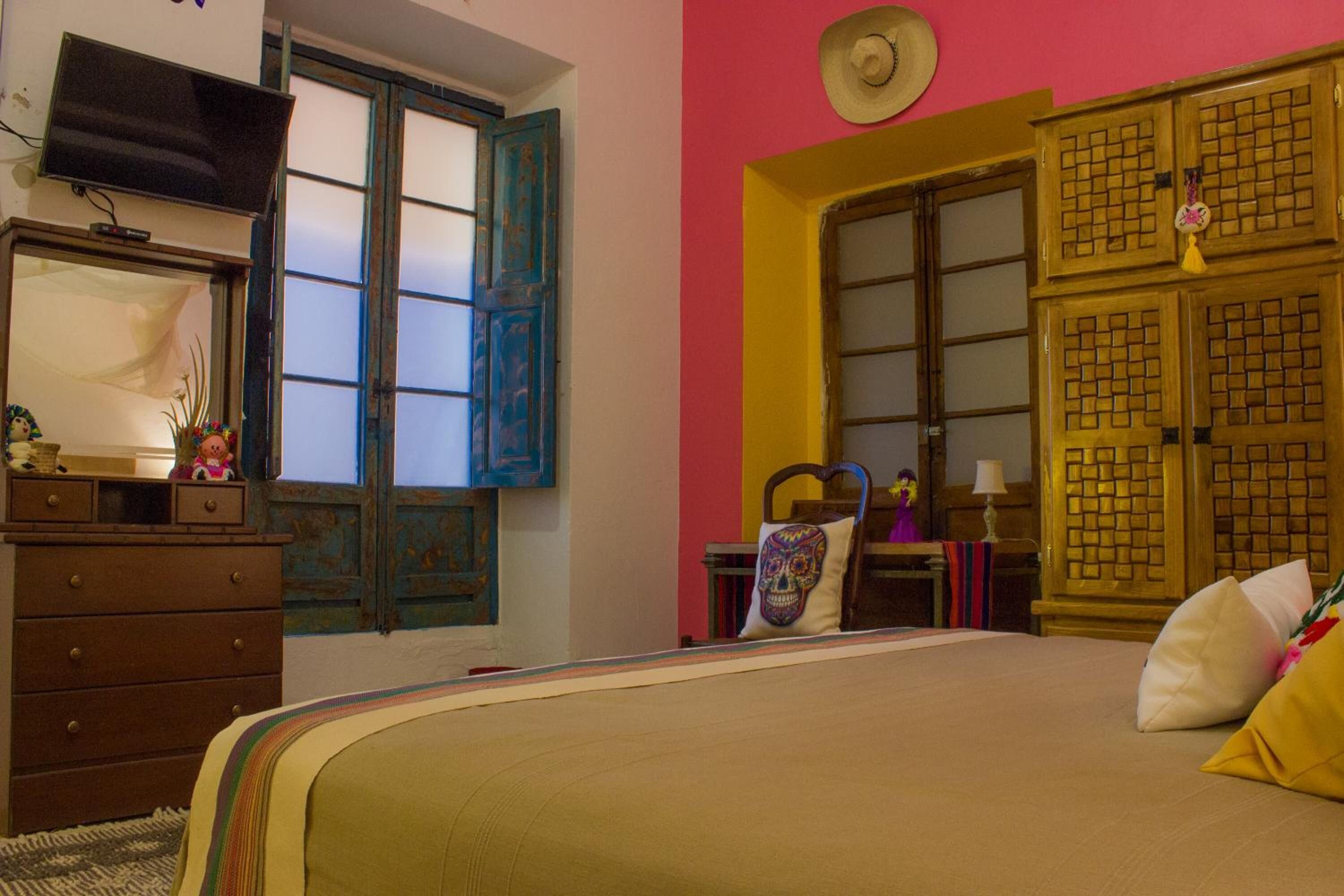 A bedroom with a bed, dresser, and a TV on a shelf.