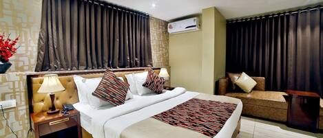 A hotel room with a large bed, bedside tables, a sofa, an air conditioning unit, and a decorative wall pattern.