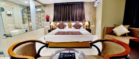 Una habitación de hotel con una cama grande, dos sillones, una mesita y un separador de vidrio.