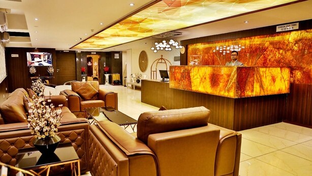 Um hall de hotel com sofás de couro, um balcão de recepção e uma tela digital grande.