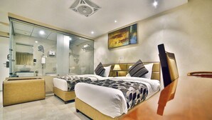 Quarto de hotel moderno com duas camas, box de vidro, mesa de cabeceira e uma pintura grande na parede.
