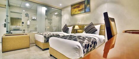 A modern hotel room with two beds, a glass shower enclosure, a bedside table, and a large painting on the wall.