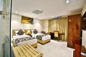 Habitación de hotel con dos camas, un escritorio, una silla, un televisor y una ventana con cortinas.