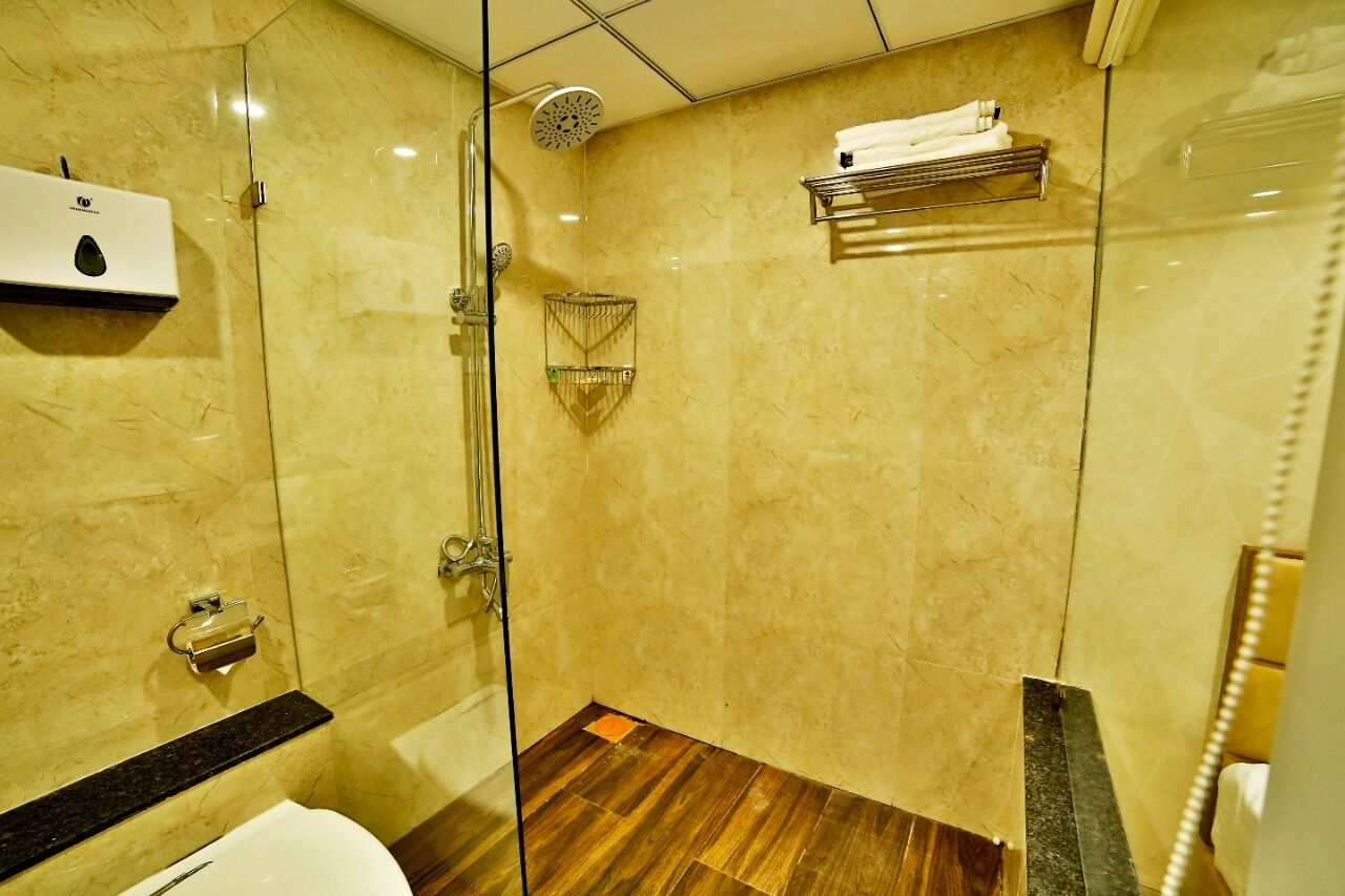 Une salle de bain moderne dotée d’une douche à parois de verre, d’un mur recouvert de carreaux de marbre, d’un plancher en bois et d’une étagère intégrée où est posée une serviette.