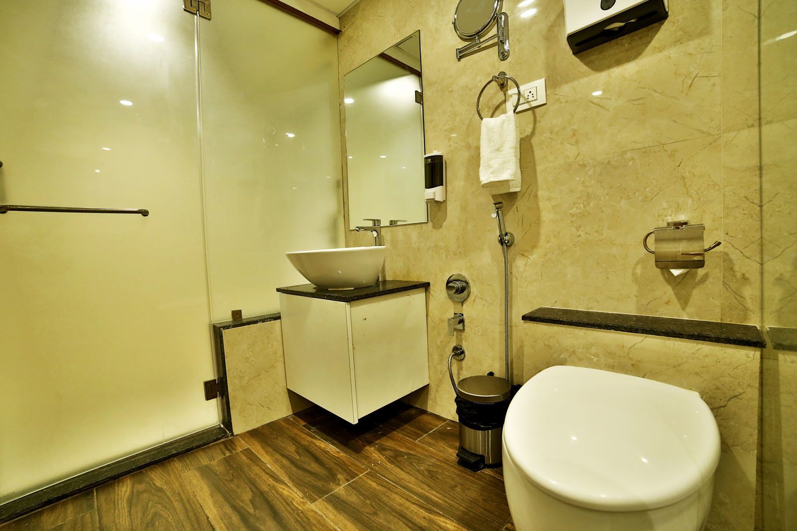 A modern bathroom with a glass shower enclosure, a white sink with a vessel basin, a toilet, and a towel rack.
