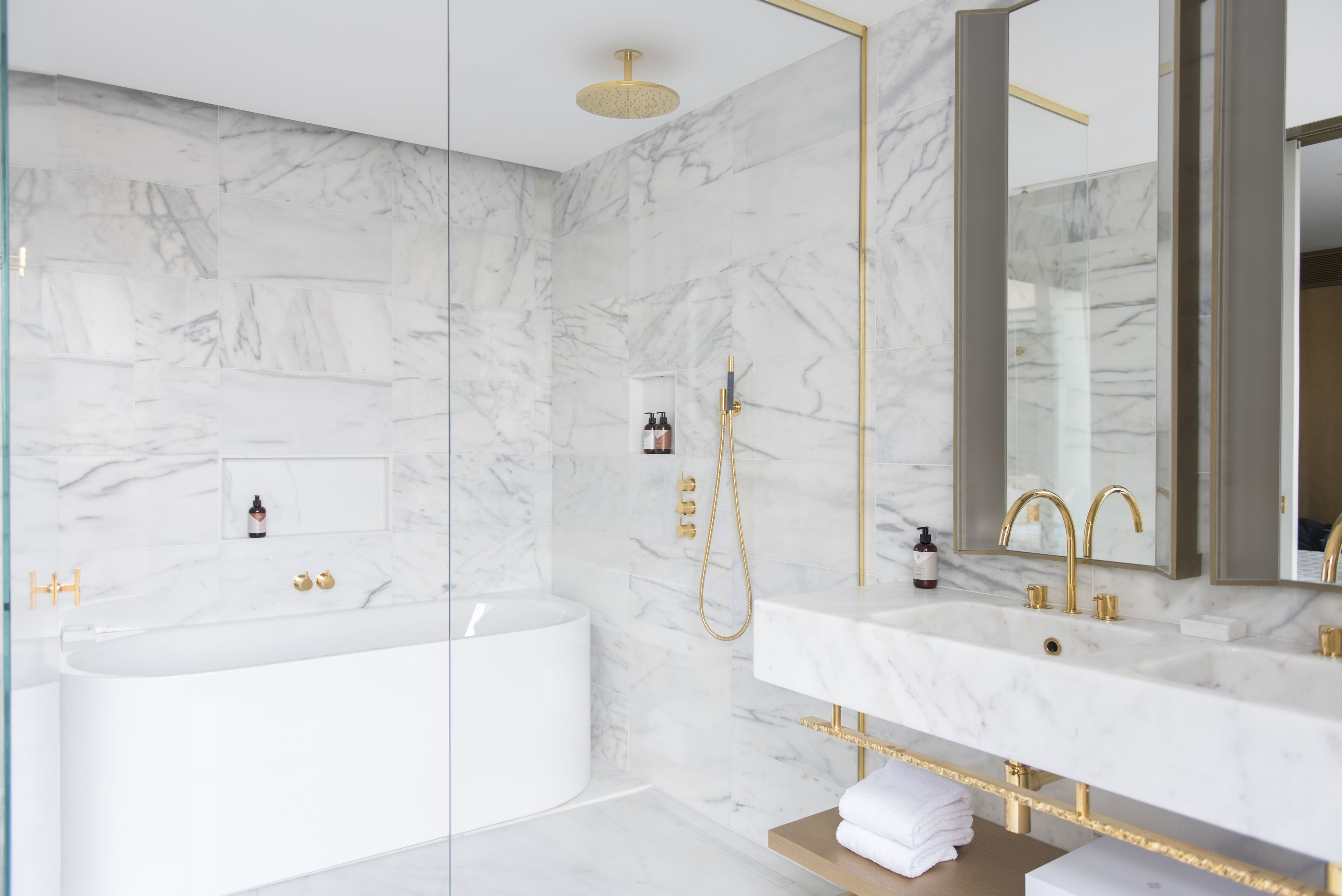 Een moderne badkamer met een vrijstaand bad, een wastafel met gouden details en marmeren wanden.