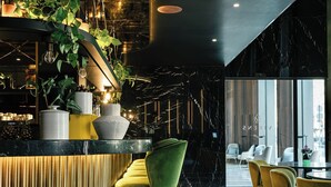 A modern bar area with a curved counter, green and yellow chairs, and potted plants. - Almanac Barcelona (Barcelona)