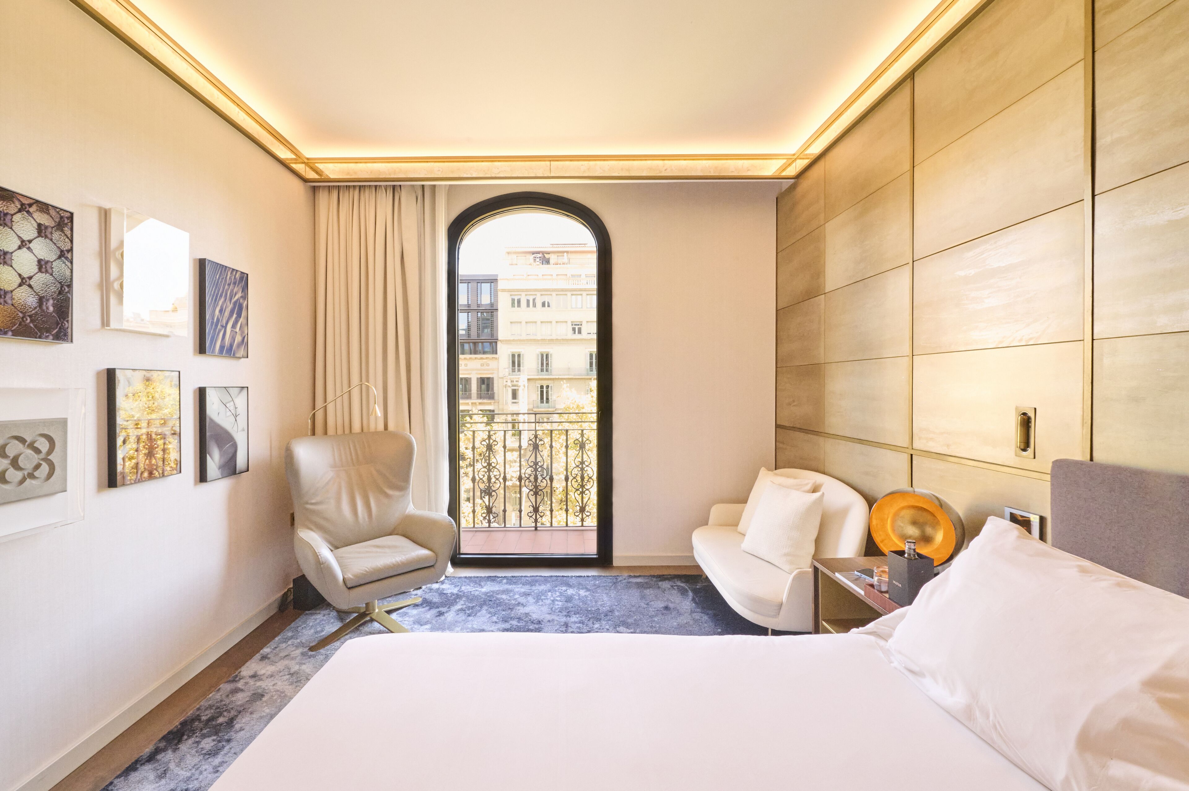 Une chambre d’hôtel avec un grand lit, une chaise, une petite table avec une lampe et une vue sur les bâtiments par la fenêtre.