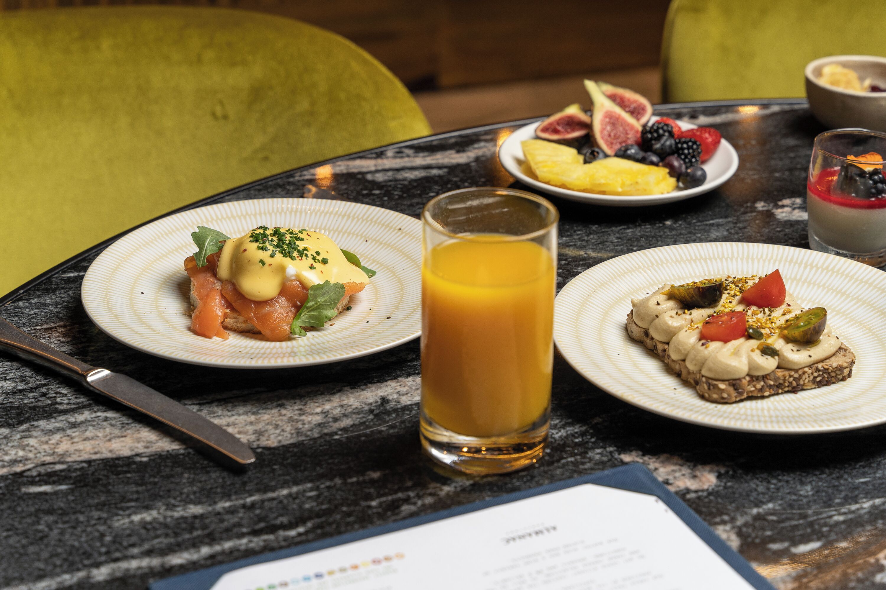 A breakfast setting with plates of food, a glass of orange juice, and a menu on a table.